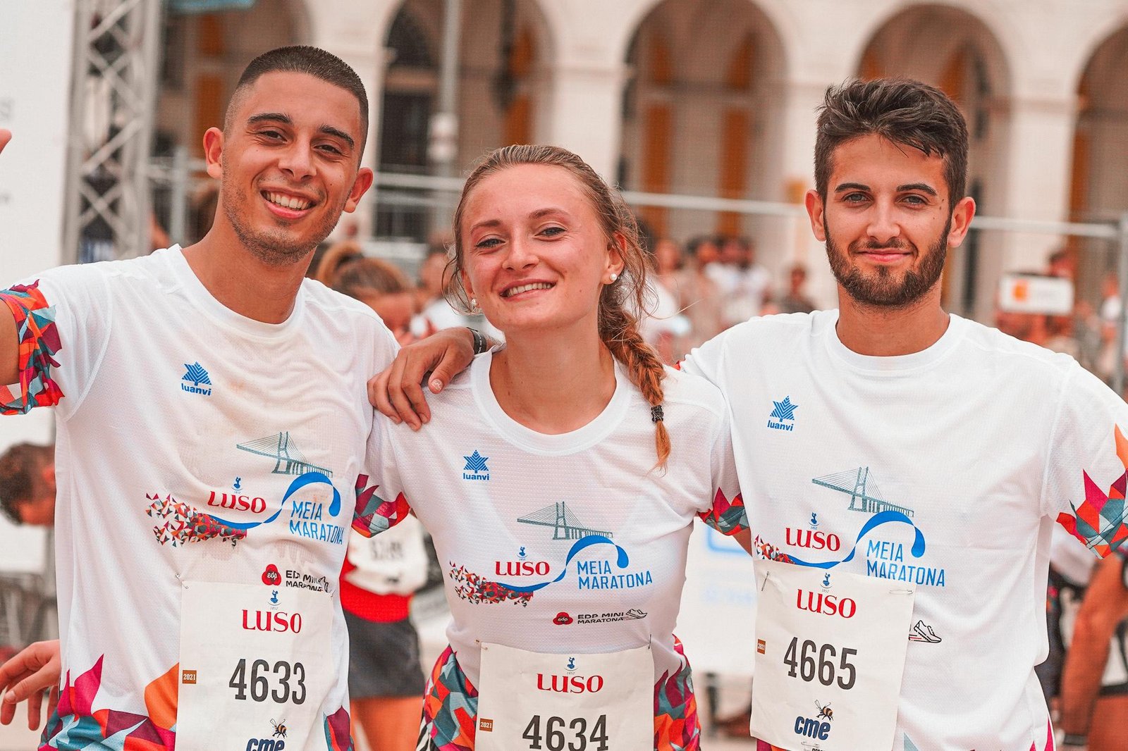 Group of three smiling runners after finishing a marathon, celebrating together outdoors.
